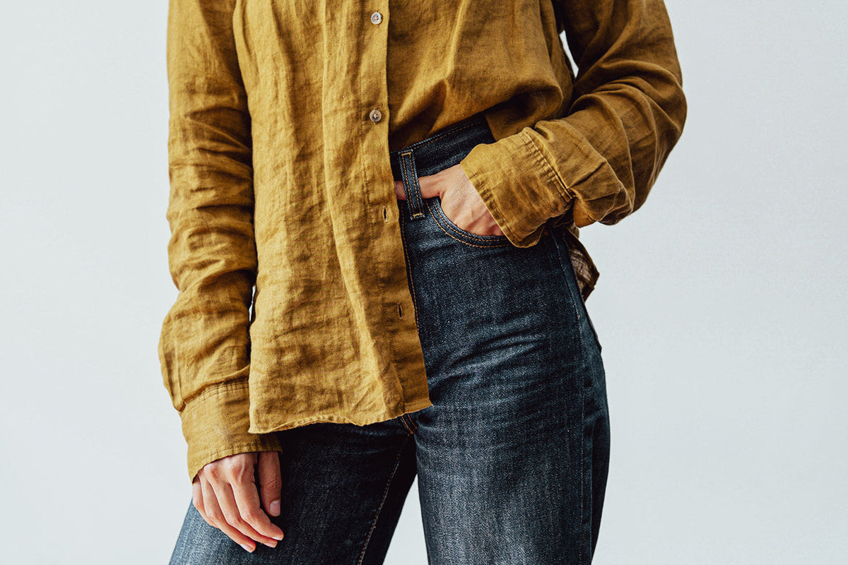 Person wearing a mustard yellow shirt and dark jeans against a plain background